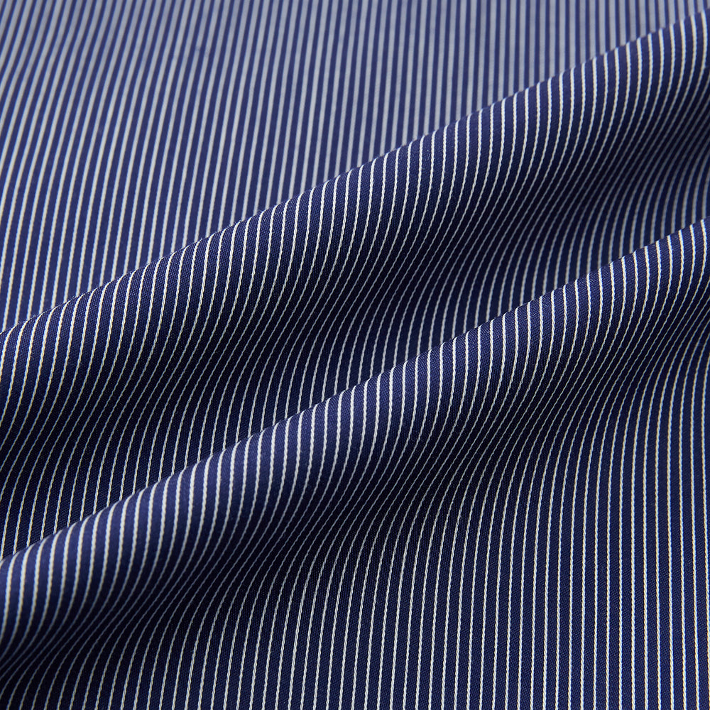 The Navy Stripe Highbury Overshirt by Turnbull & Asser features thin vertical stripes, black buttons, a collar, and a chest pocket. Displayed on a plain white background, it’s inspired by classic Turnbull & Asser style.