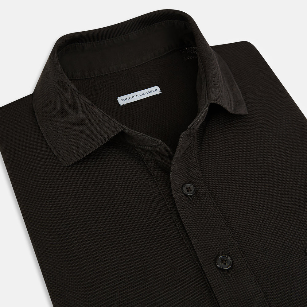 A brown short-sleeve polo shirt by Turnbull & Asser, crafted from pure cotton jersey with a collar, three buttons, and a buttoned chest pocket, laid flat on a white background.