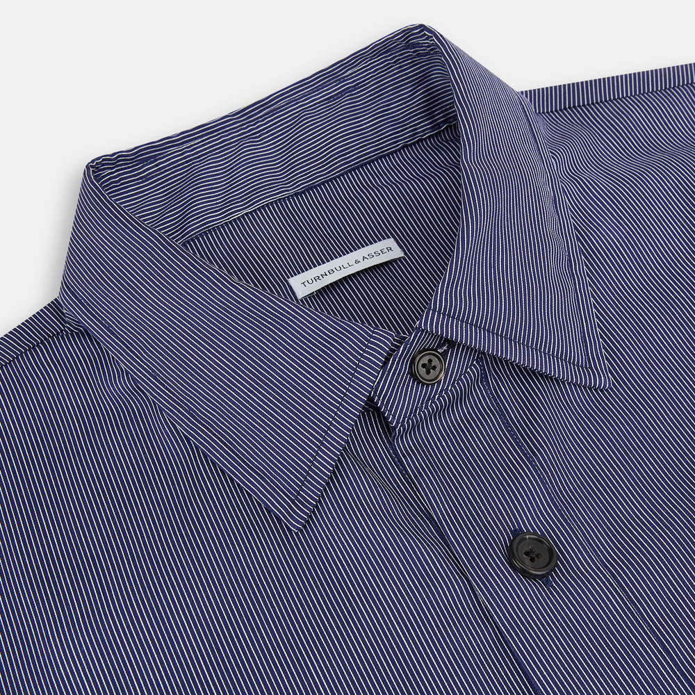 The Navy Stripe Highbury Overshirt by Turnbull & Asser features thin vertical stripes, black buttons, a collar, and a chest pocket. Displayed on a plain white background, it’s inspired by classic Turnbull & Asser style.