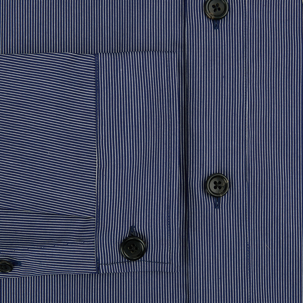 The Navy Stripe Highbury Overshirt by Turnbull & Asser features thin vertical stripes, black buttons, a collar, and a chest pocket. Displayed on a plain white background, it’s inspired by classic Turnbull & Asser style.